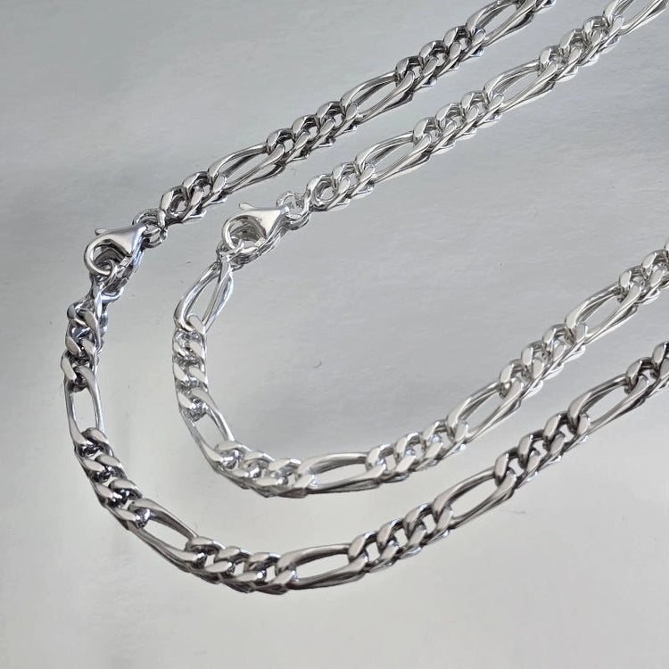 Comparaison visuelle entre chaîne homme argent massif rhodié (plus sombre) et argent massif blanc (traditionnel) maille Figaro 3 mm alternée.