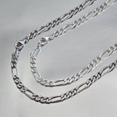 Comparaison visuelle entre chaîne homme argent massif rhodié (plus sombre) et argent massif blanc (traditionnel) maille Figaro 3 mm alternée.