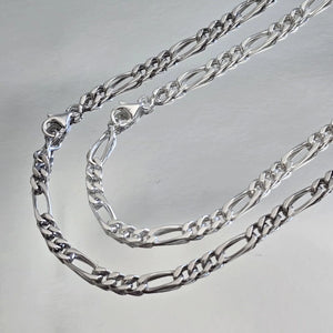 Comparaison visuelle entre chaîne homme argent massif rhodié (plus sombre) et argent massif blanc (traditionnel) maille Figaro 3 mm alternée.